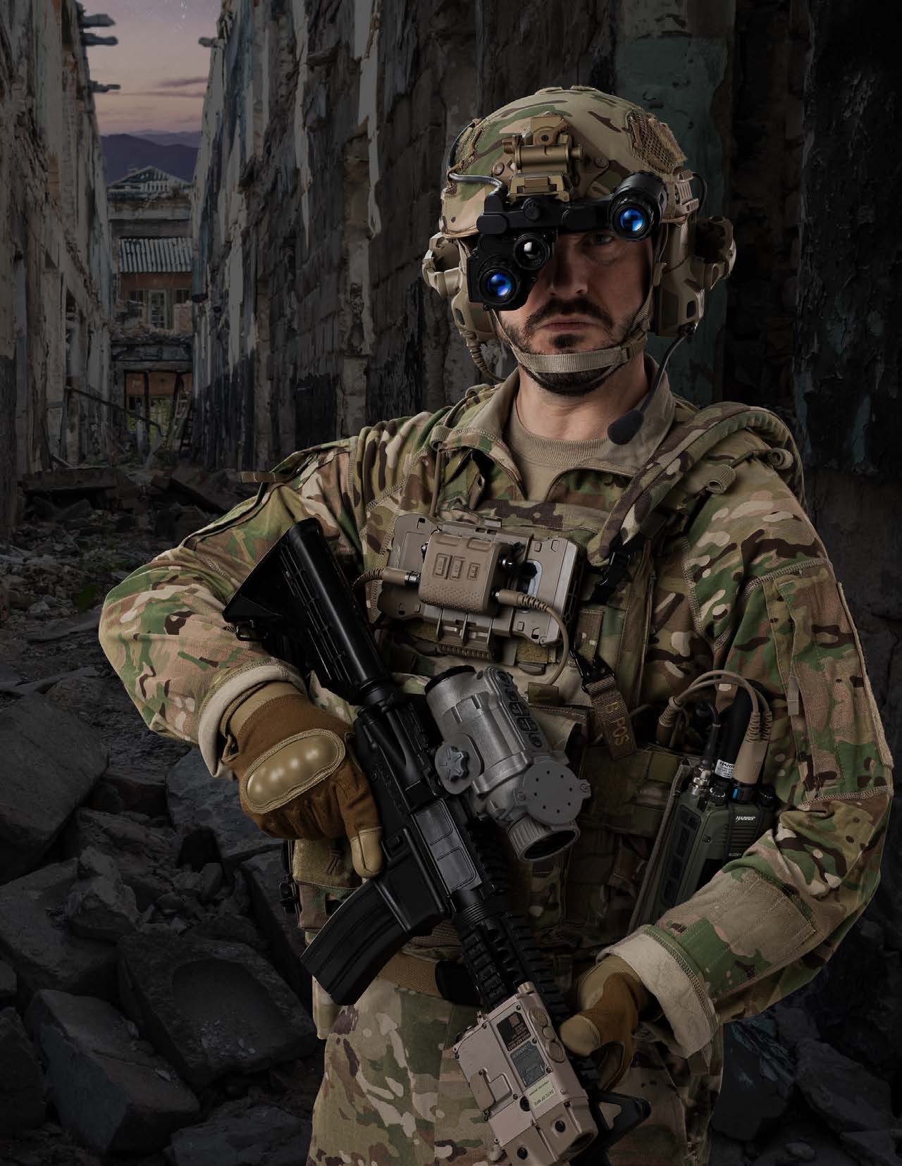A soldier in urban ruins wearing the Integrated Soldier System: panoramic night vision goggles, a chest-mounted display, a thermal weapon sight on the rifle, and a tactical radio