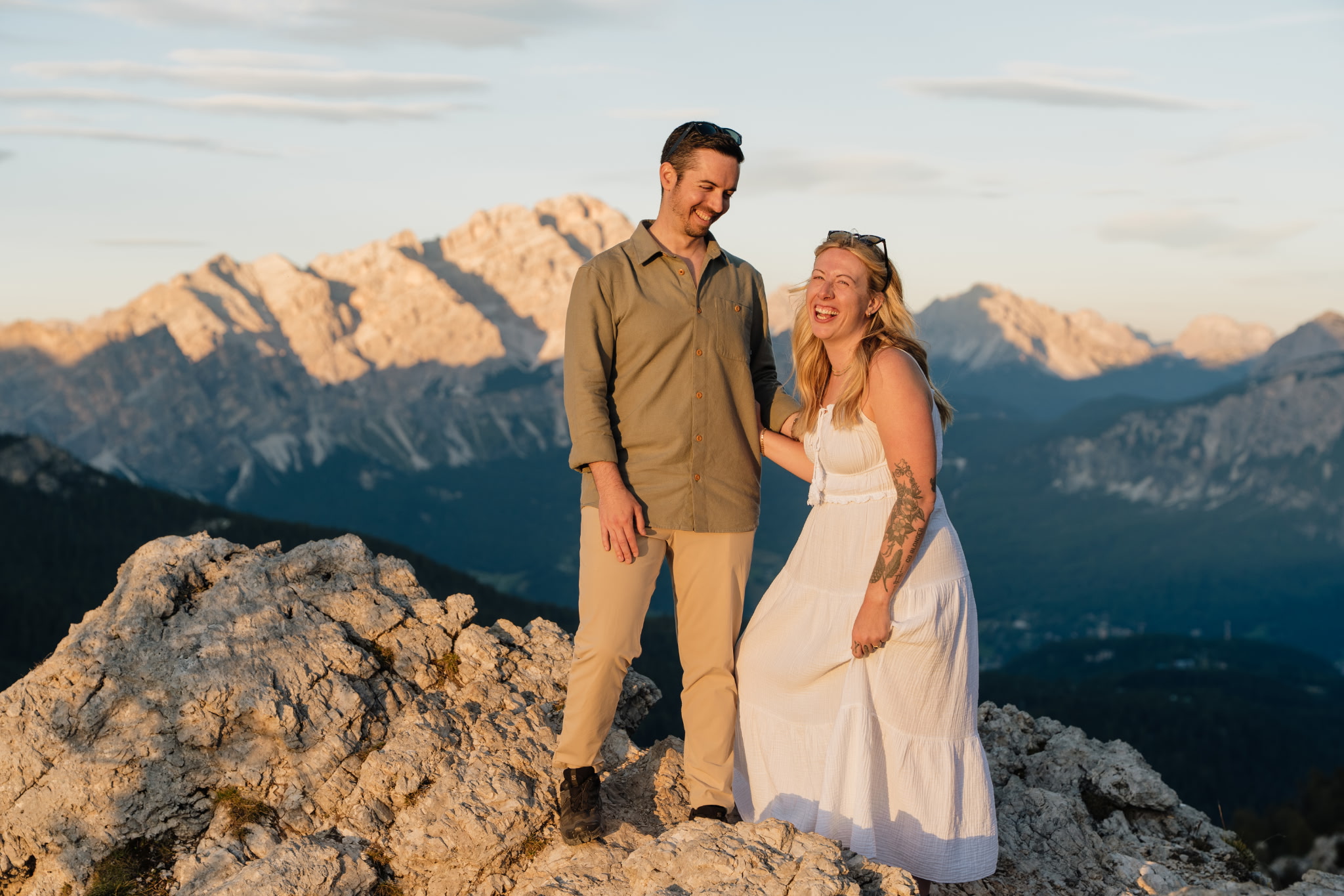Eric and his wife laughing together on a rocky summit at golden hour, with the Dolomite mountains of Northern Italy behind them